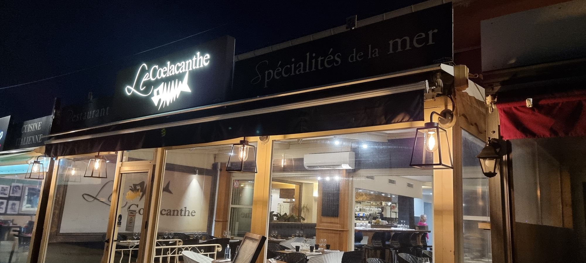 La façade du restaurant de nuit, enseigne lumineuse et vitrines éclairées