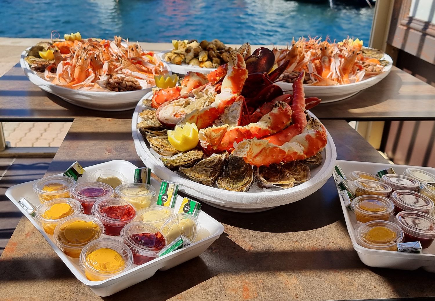 Un grand plateau de fruits de mer posé sur une table de terrasse, avec ses sauces, au soleil