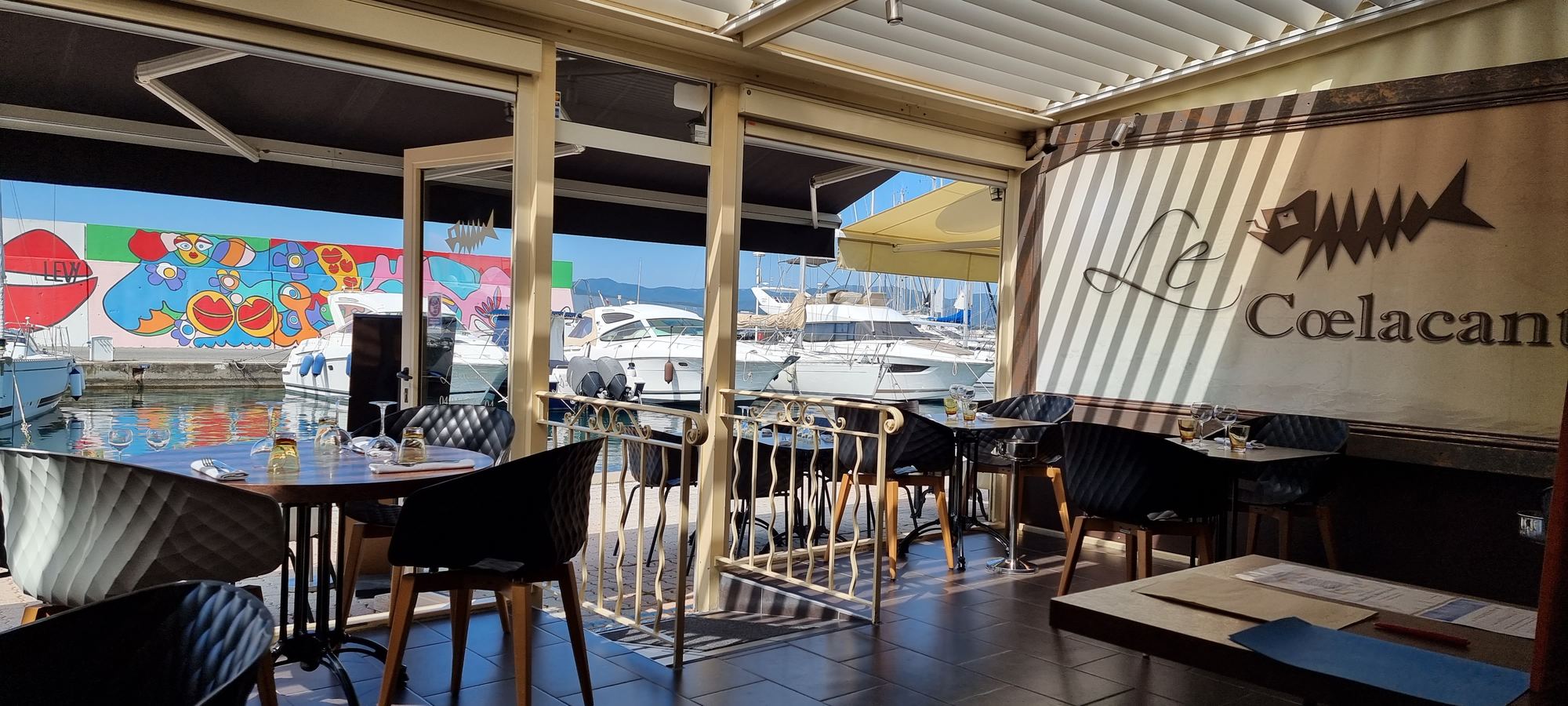 La terrasse vitrée du restaurant, ses tables et, derrière, les bateaux amarrés du port de Santa Lucia